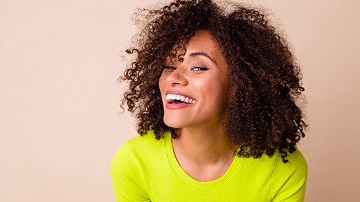 Woman with chartreuse sweater smiling with beige background