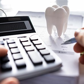 Fingers holding pen and touching calculator at desk with invoice and model tooth