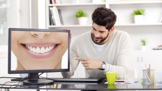 Man pointing to computer monitor showing close up of flawless smile