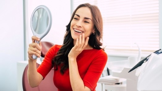 Young woman admiring her smile in mirror after cosmetic dentistry