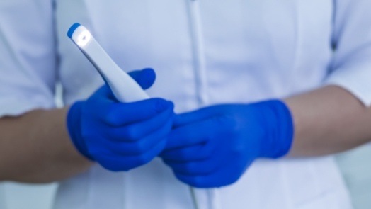 Two gloved hands holding a thin white intraoral camera