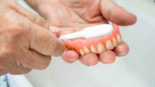 Person cleaning their denture with a toothbrush
