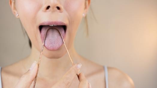 Woman using tongue scraper for dry mouth treatment in Tulsa