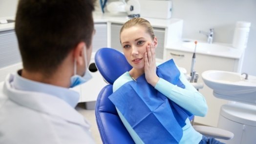 Woman holding her cheek in pain while talking to emergency dentist in Tulsa