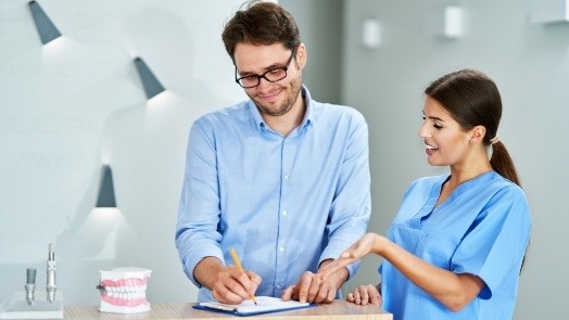 Dental team member showing man where to sign on clipboard