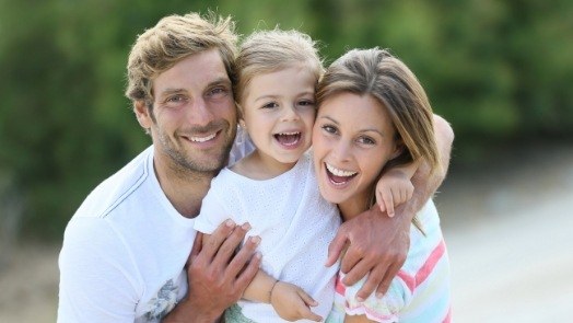 Mother father and young child grinning outdoors