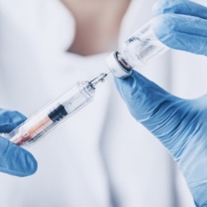 Medical professional drawing a syringe from vial of clear liquid