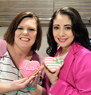 Two smiling dental team members holding heart shaped cookies