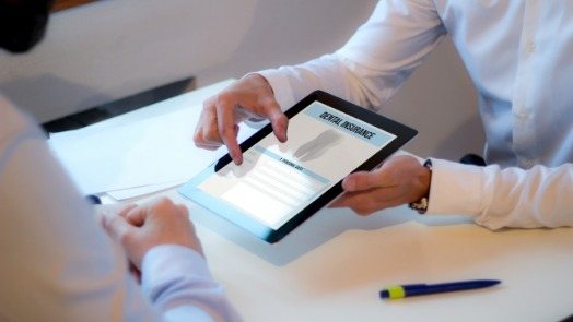 Two people looking at tablet with dental insurance information at table