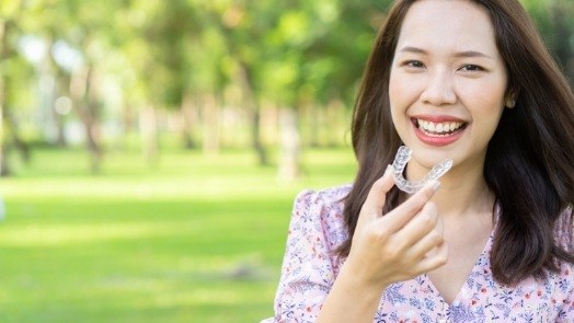 Smiling woman holding Invisalign aligner outdoors