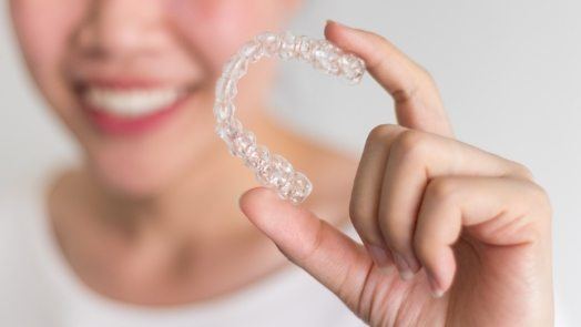 Smiling person holding Invisalign clear aligner