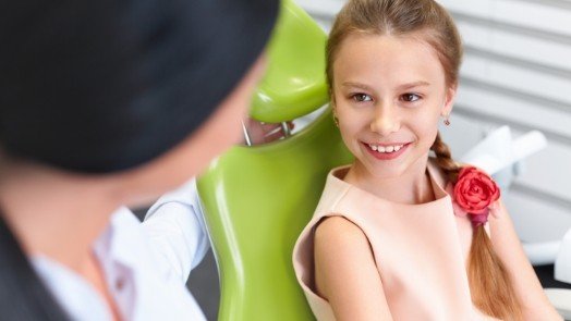 Young girl in dental chair smiling at her dentist