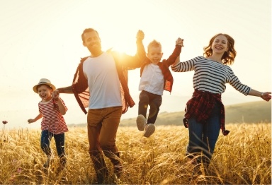 Family of four holding hands while walking through tall grass