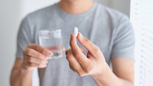 Man holding a pill and a glass of water