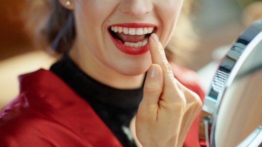 Woman with red lipstick looking at her teeth in mirror