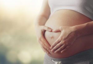 Pregnant woman making a heart shape over her belly button