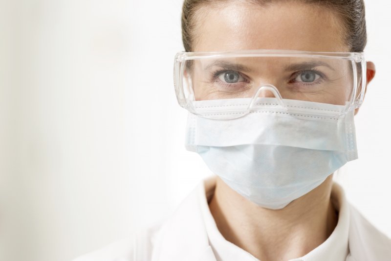 a dentist wearing protective eyewear, lab coat, and a face mask 