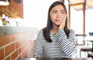 Woman hand on cheek wonders about wisdom teeth removal in Tulsa