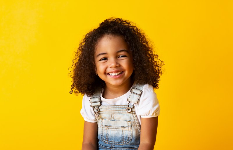 a young girl wearing denim overalls smiles after undergoing a frenectomy in Tulsa