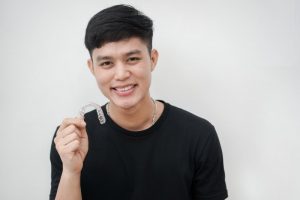 smiling young man holding an Invisalign clear aligner 
