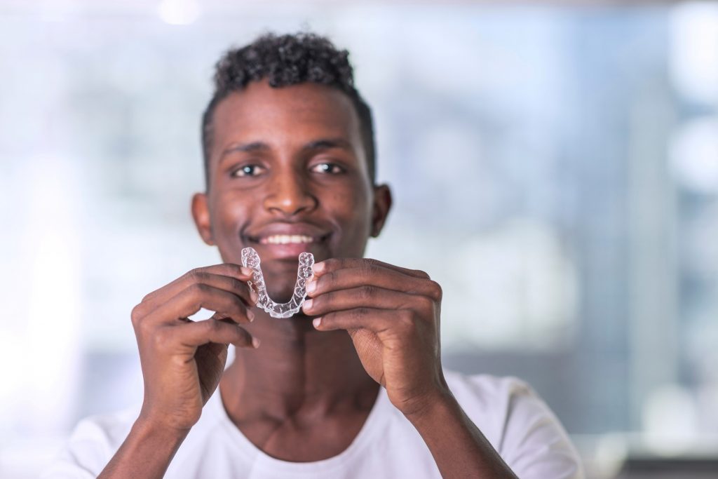 Man in white shirt smiling while holding Invisalign aligner