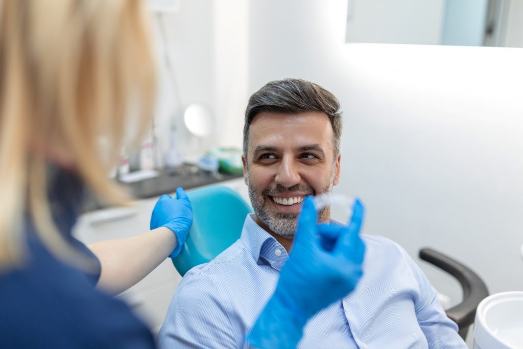 Man smiling at dentist holding Invisalign aligner