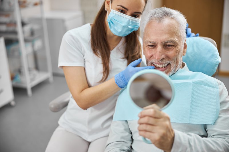 An older man looking at his new dental implant dentures in a mirror