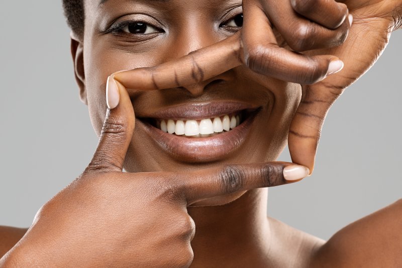 A woman smiling and framing her teeth with her fingers after her cosmetic dentistry treatments